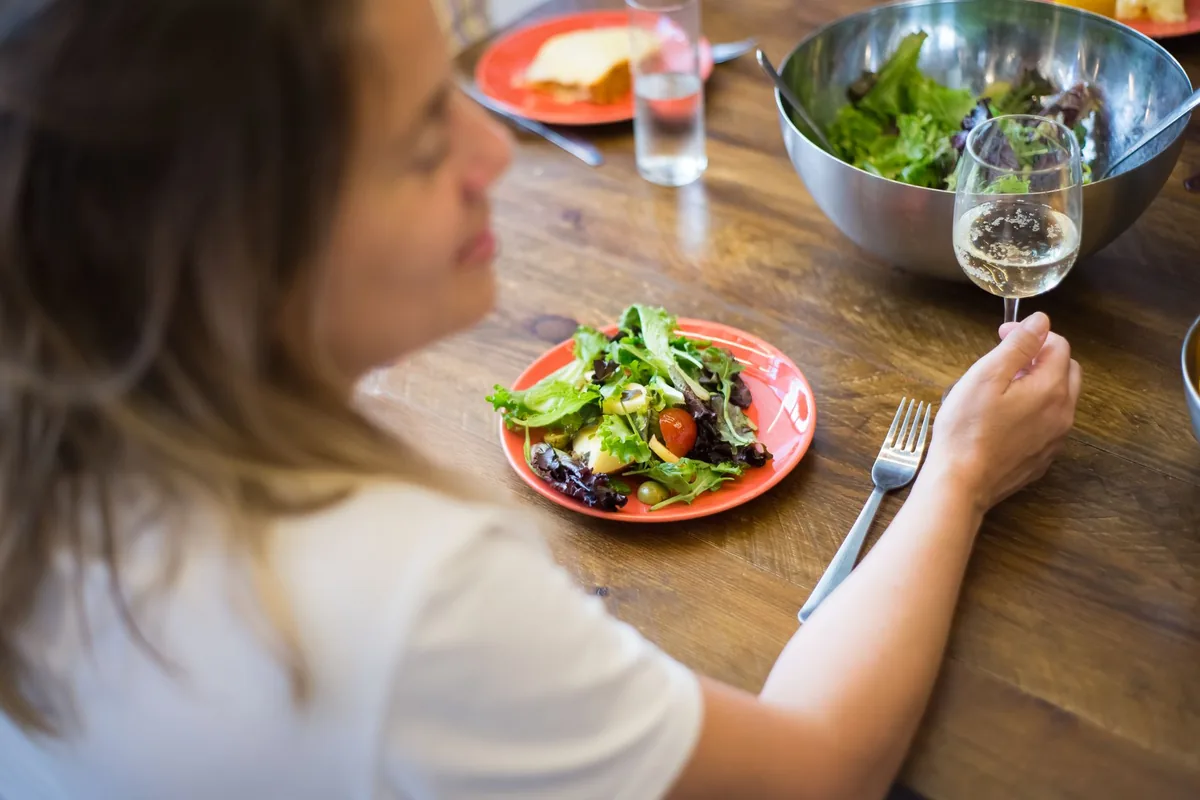 A woman eating a bowl of salad at a table