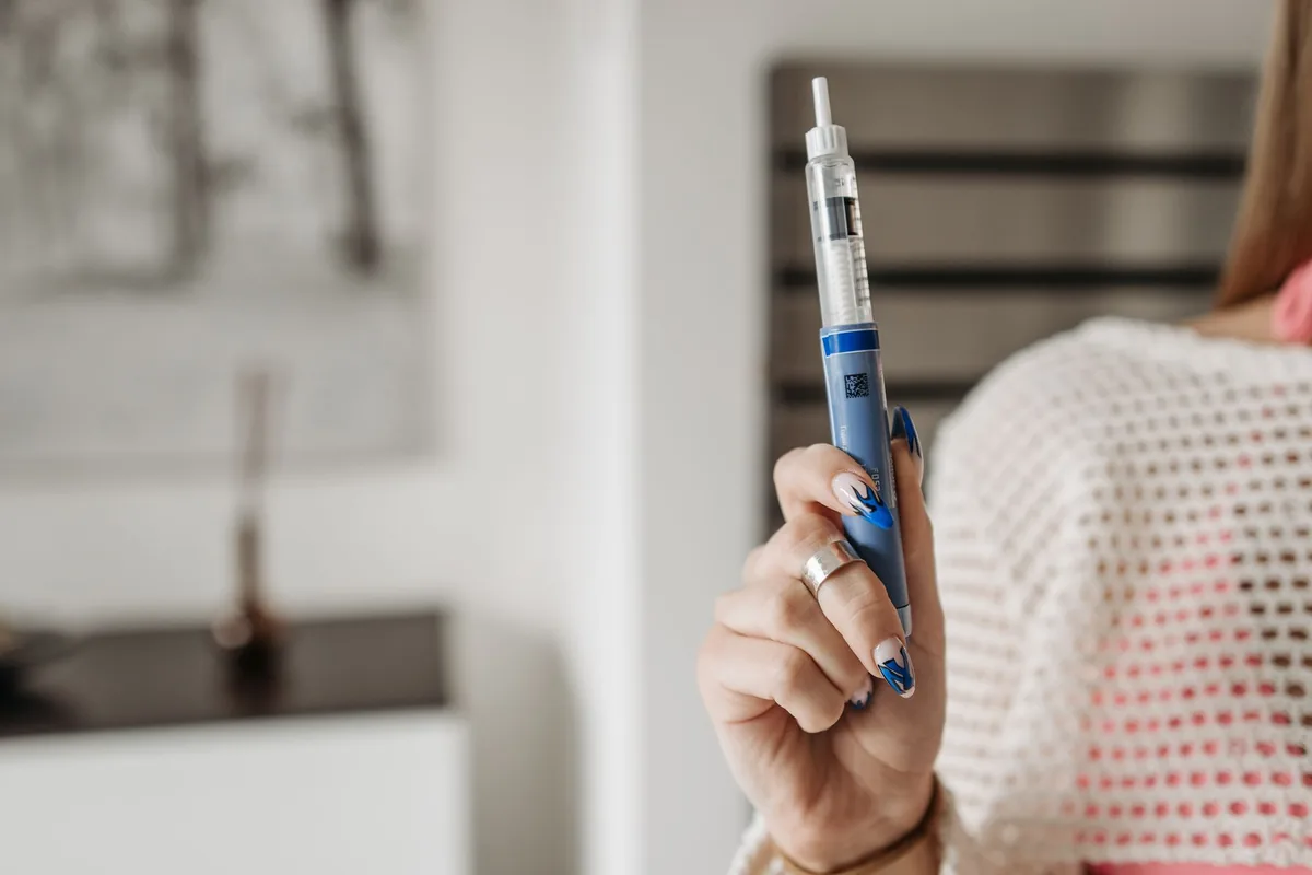 A hand holding a pen-style injector device