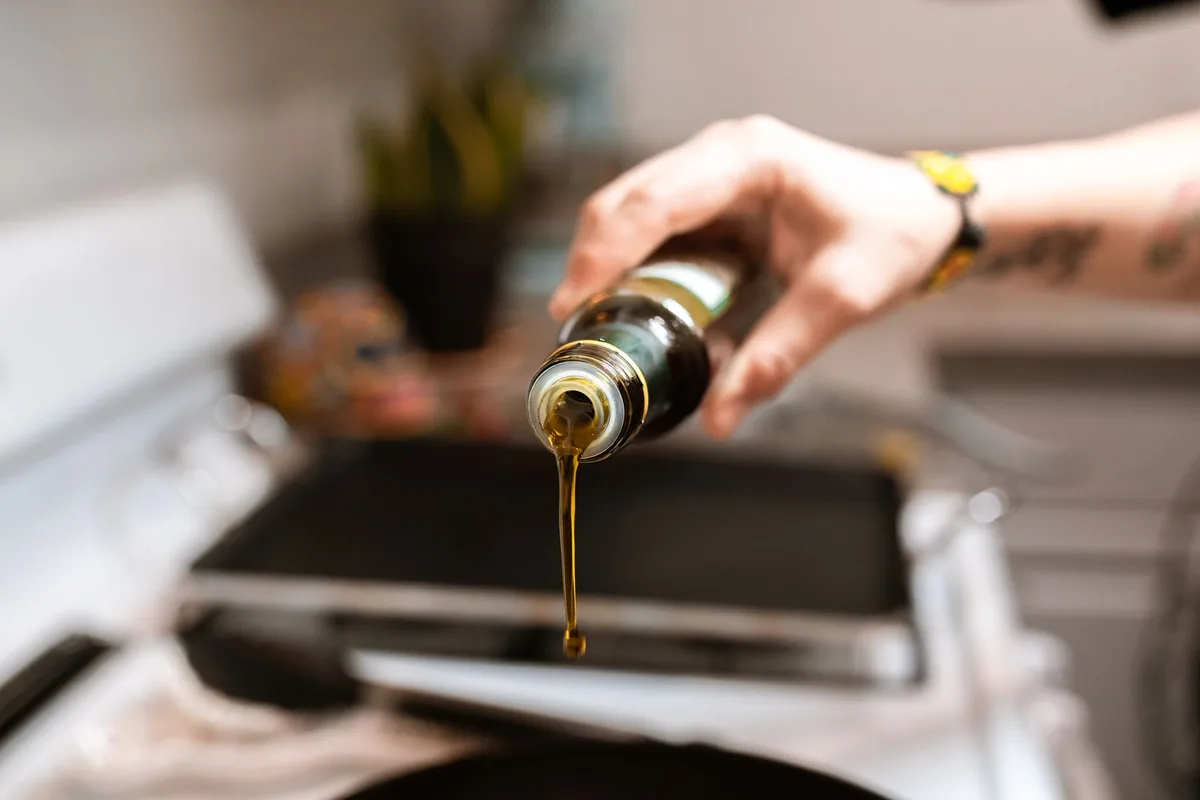 Olive oil being poured from a bottle into a frying pan