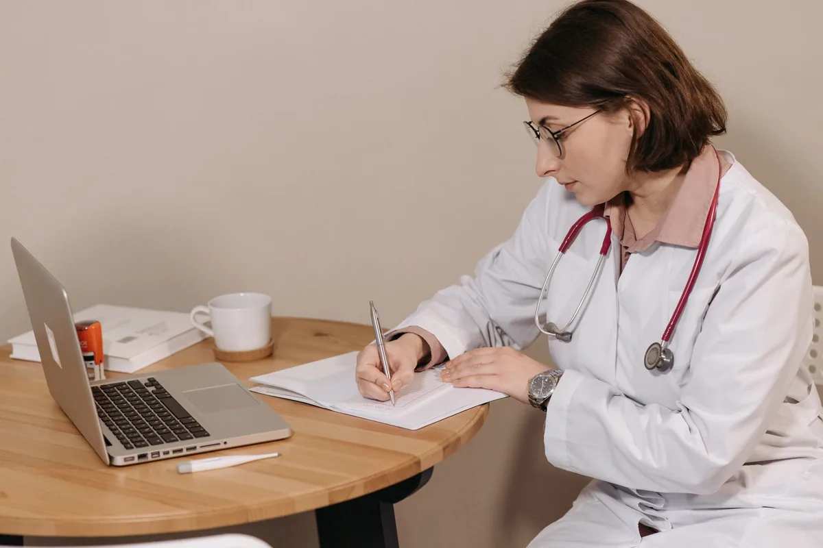 A clinician making notes at a desk with a laptop